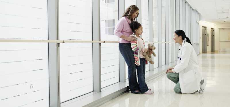 Physician kneeling to talk to a child in a hospital hallway.