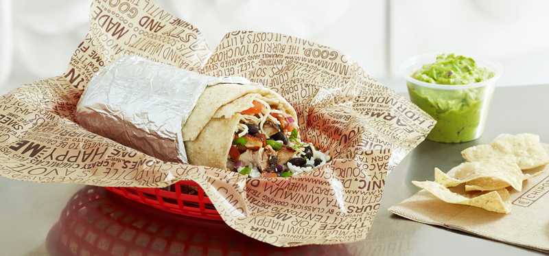 A Chipotle burrito in a basket and wrapper.
