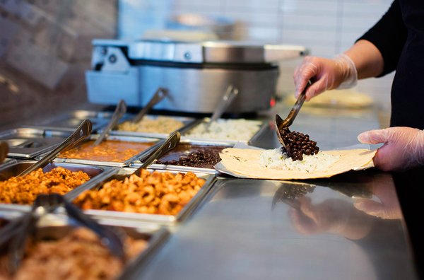 A Chipotle employee scooping ingredients into a burrito.