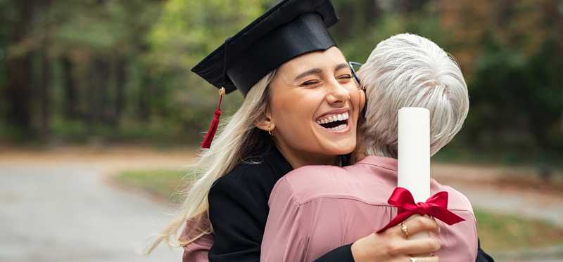 Graduate holding diploma and hugging person outside.