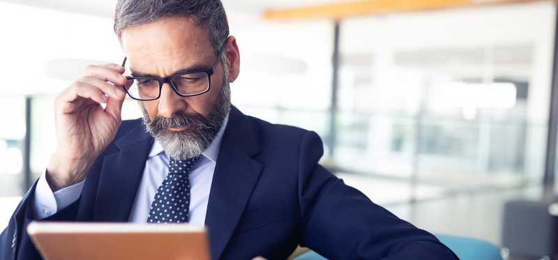Businessperson adjusts glasses while looking at tablet.
