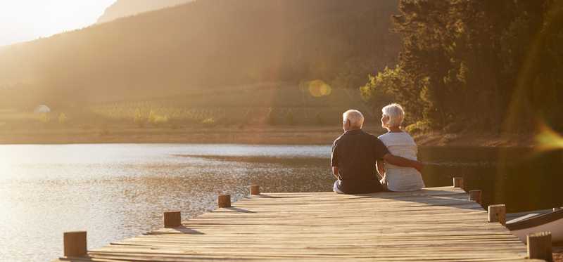 Two people sitting on a dock at a lake.