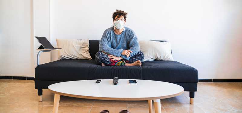 Man sitting cross-legged in pajamas with a surgical mask on his face