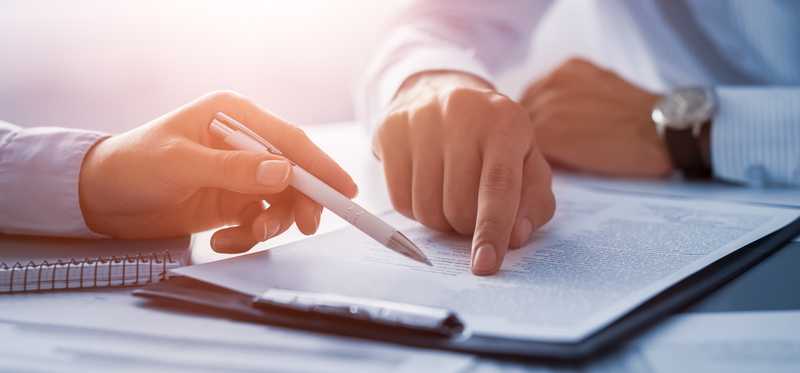 The hands of two people review paperwork on a clipboard.