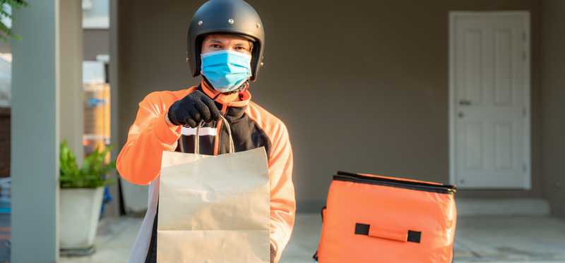 Person wearing face mask and motorcycle helmet delivering food