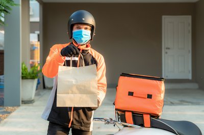 Person wearing face mask and motorcycle helmet delivering food