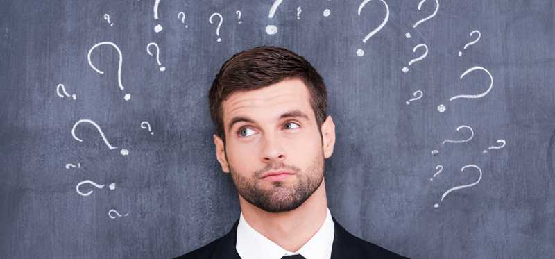 Confused man question standing in front of chalkboard with question marks drawn around his head