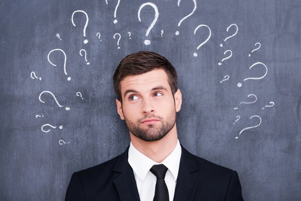 Confused man question standing in front of chalkboard with question marks drawn around his head