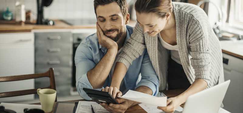 Two smiling people review paperwork at home in front of laptop.