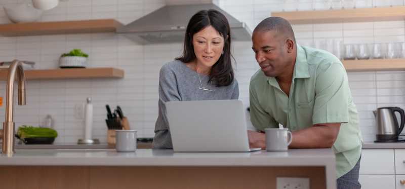 Two people in kitchen looking at laptop.