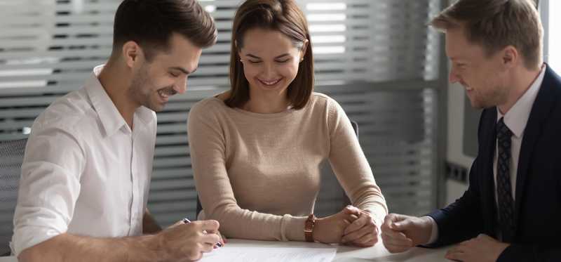 Two people signing forms for a third person in a suit and tie.