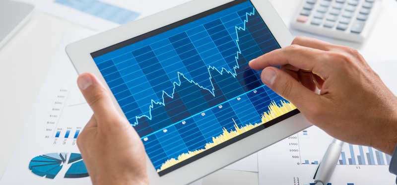 Hands holding a tablet and inspecting a line graph on its screen.