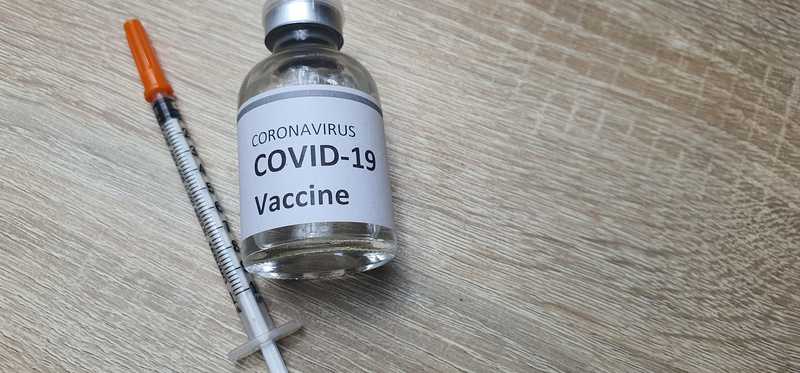 A hypodermic needle and a vial that says COVID-19 vaccine.