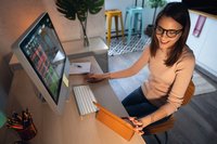 Person smiles while seated at desk in front of large monitor with financial charts.