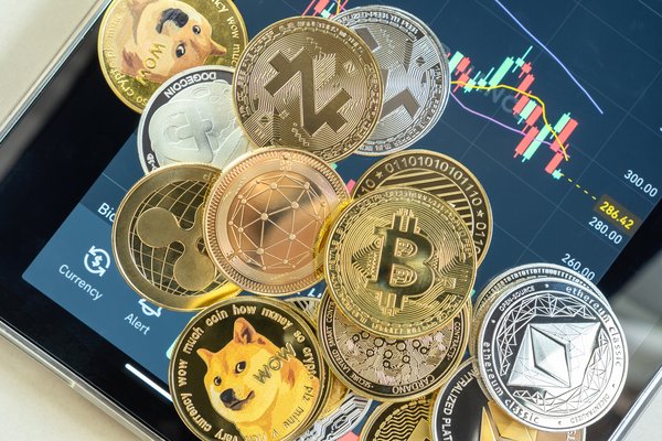 Different cryptocurrencies lying in a pile atop a smartphone opened to a trading app.