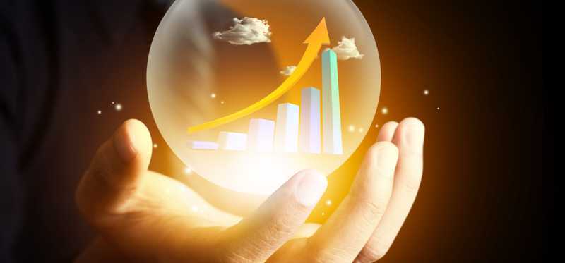 Person holding crystal ball with financial markets trending upward.