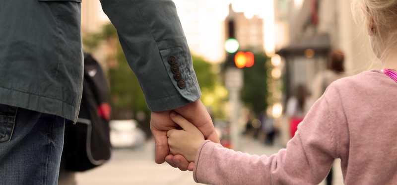 Adult and child holding hands walking downtown.