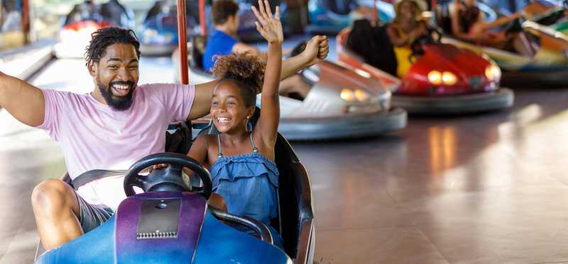 An adult and a child in a bumper car, hands in the air.