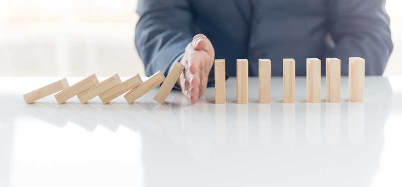 A hand stops dominos from being knocked down.