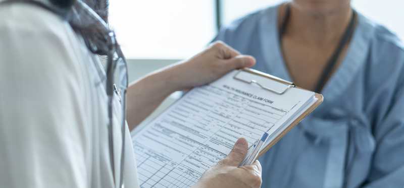 Doctor holding insurance claims form and talking with patient in hospital gown