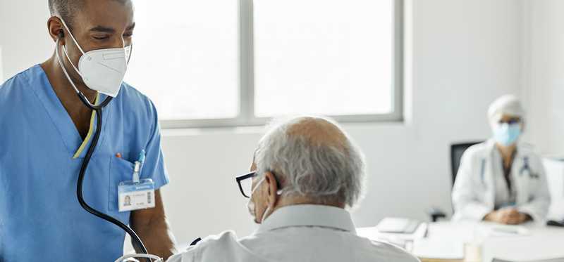 Doctor in scrubs taking heart rate of patient.