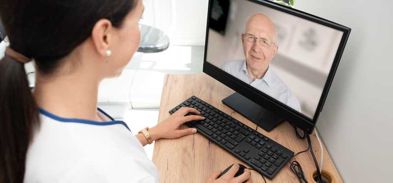 A medical professional talking to a patient on a laptop screen.