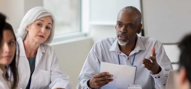 Doctors sitting at conference room table discussing paperwork.