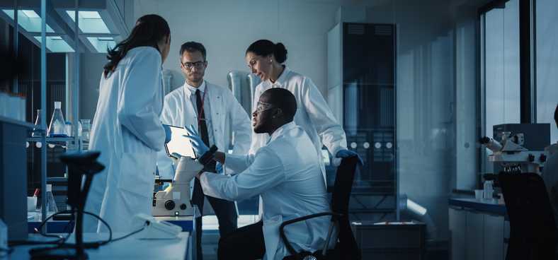 Four people in white jackets working together in a laboratory.