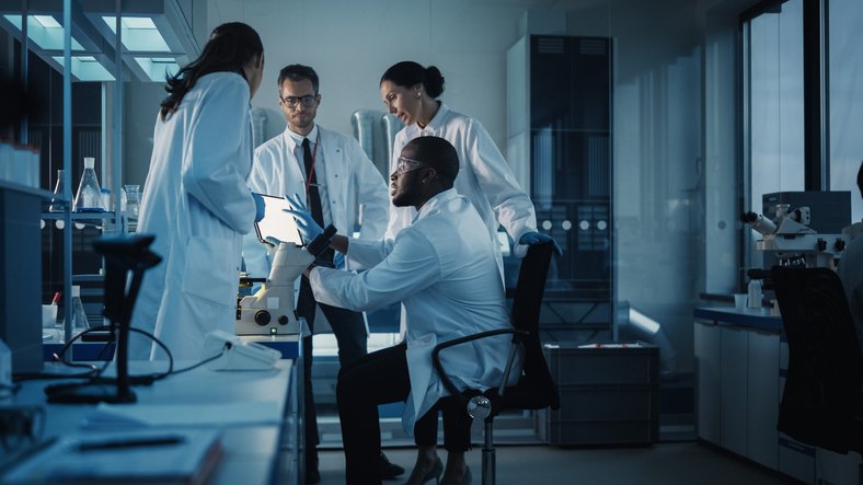 Four people in white jackets working together in a laboratory.