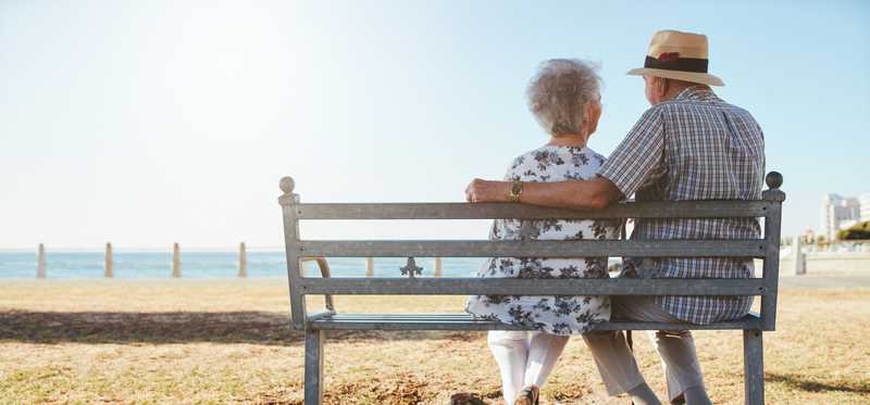 Two people sitting on a bench on the beach.