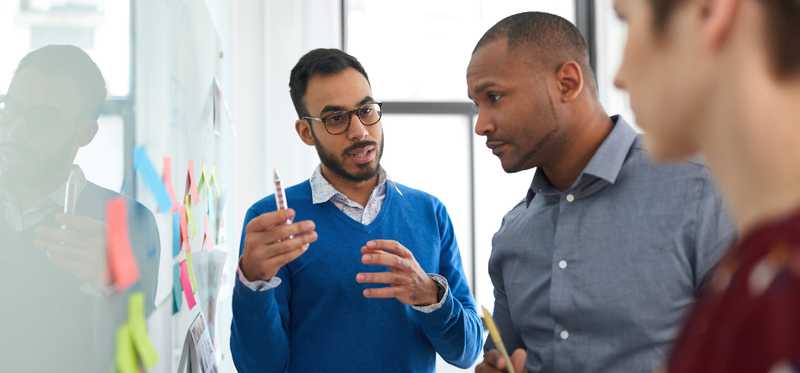 Employees collaborate in front of wall of Post-it notes.