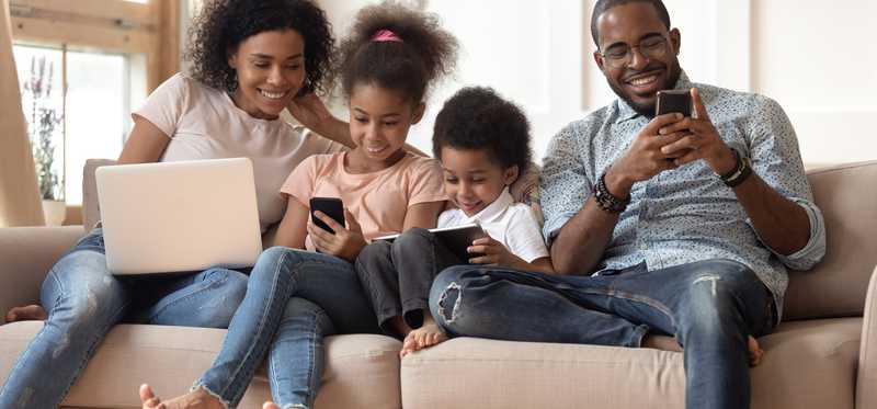 Family sitting on couch with electronics in hand