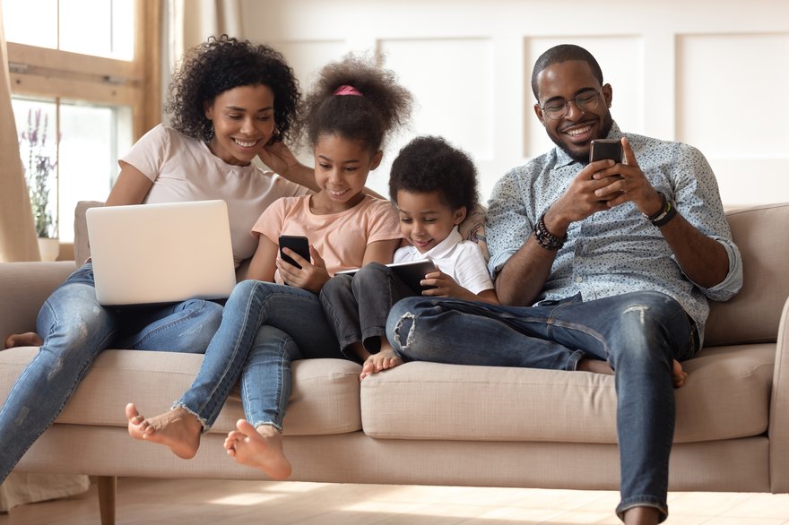 Family sitting on couch with electronics in hand