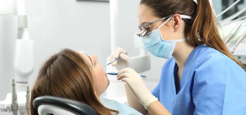 Female dental hygienist cleaning female patient's teeth.