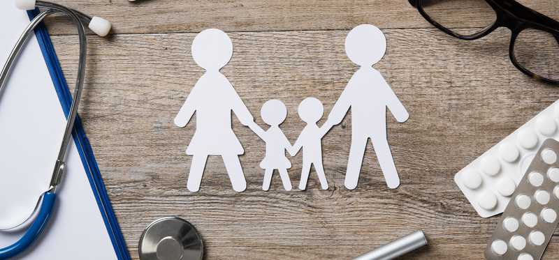 Paper cutout of family next to stethoscope, pills, and glasses.