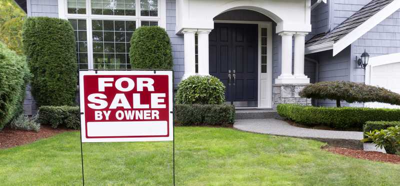 House with a sign in front yard that says For Sale by Owner.