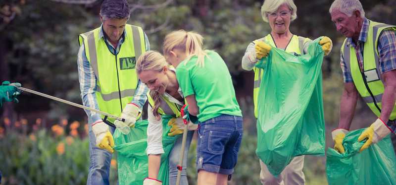 four adults and young girl carrying trash bags and picking up litter