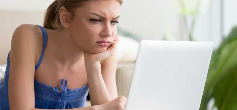 Young woman with look of frustration on her face looking at her laptop screen.