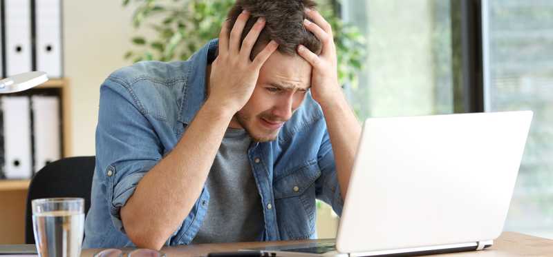 Frustrated person holding their hands to their head and looking at laptop screen.