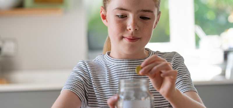Child puts coins into glass jar.