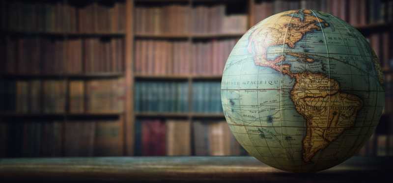 A globe on a table in front of a bookcase.