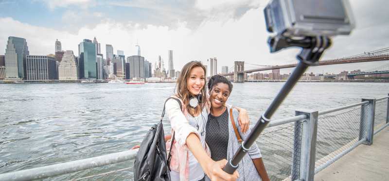Two female tourists use a camera on a stick to take a photo.