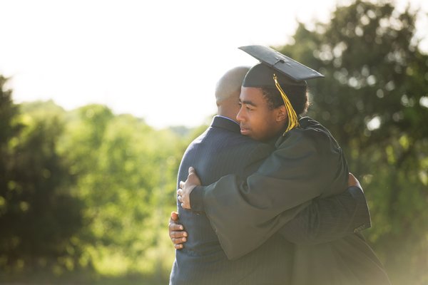 Graduate in cap and gown hugs family member.