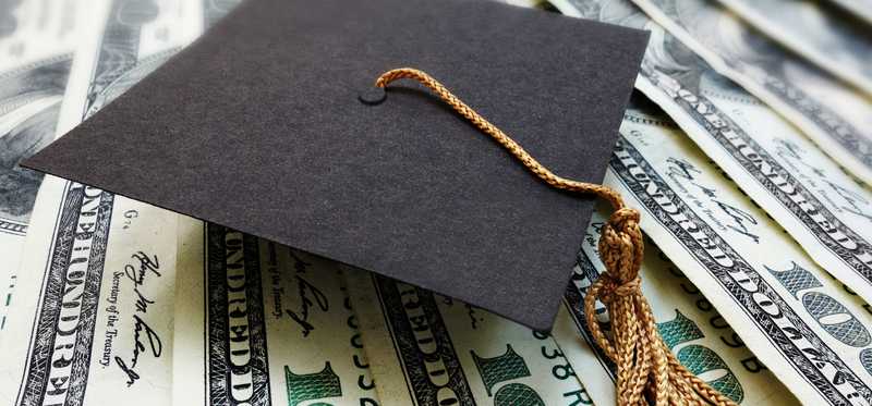 Graduation cap on a pile of hundred dollar bills.
