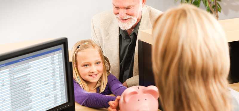 Two adults and a child with a piggy bank in a business setting.