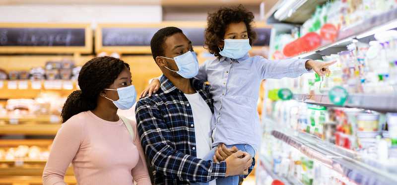 Two adults and a child wearing masks and grocery shopping.