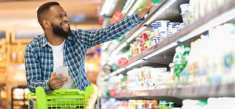 Smiling person pushing a shopping cart in a grocery store..