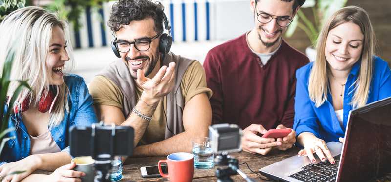 Group of friends laughing and smiling while sitting at table with photo equipment and laptop.