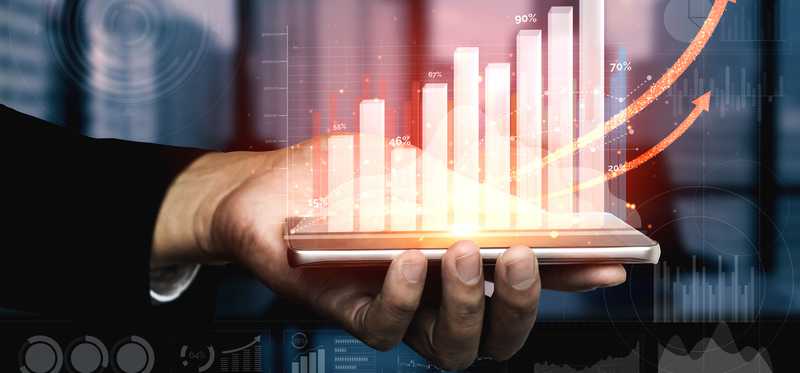 Hand holding financial markets indicator showing assets trending upward.