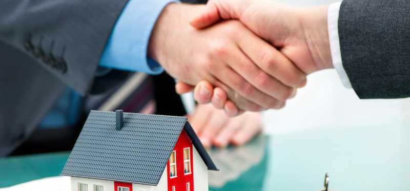 Two people shaking hands over a document and a model home